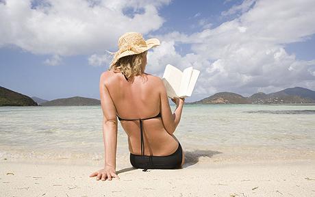 Woman on beach reading book, rear view